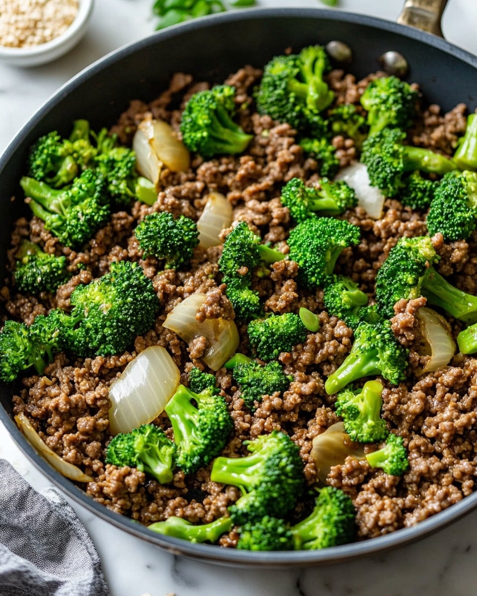 Ground Beef and Broccoli Stir Fry, beef broccoli stir fry recipe, quick ground beef meals, easy weeknight dinner ideas, healthy stir fry recipes A white bowl filled with a layered dish featuring light brown cooked rice as the base, topped with pieces of dark brown cooked ground meat scattered throughout. Bright green broccoli florets and slices of red bell pepper are mixed in with the meat and rice, adding vibrant color. Small sprinkled white sesame seeds are visible on top, along with chopped green onion pieces for garnish. The bowl is placed on a white marbled surface with a beige cloth nearby and a small white bowl with sesame seeds in the background.