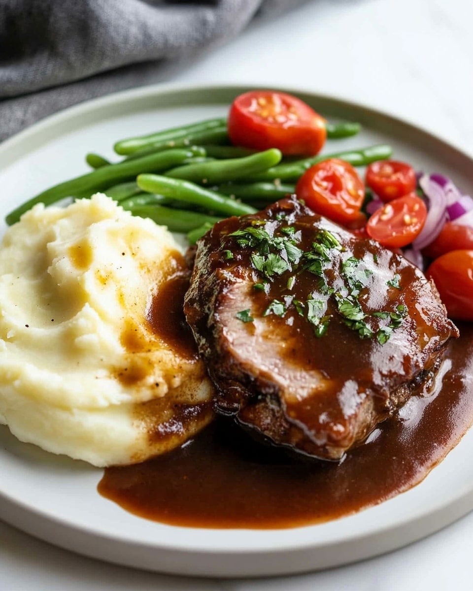 Oven Baked BBQ Chicken, homemade barbecue sauce, easy BBQ chicken recipe, juicy baked chicken with barbecue, smoky grilled chicken in oven A close-up image of a dish with three main layers on a white plate set against a white marbled surface. The bottom layer is smooth mashed potatoes, creamy and pale yellow in color. Above that lies a thick piece of cooked meat with a juicy, slightly pink interior and a dark brown glazed outer layer topped with small green herbs. On the side, a fork lifts a slice of the meat, showing its moist texture and glossy sauce dripping down. In the blurred background, there are halved cherry tomatoes and green beans adding splashes of red and green.