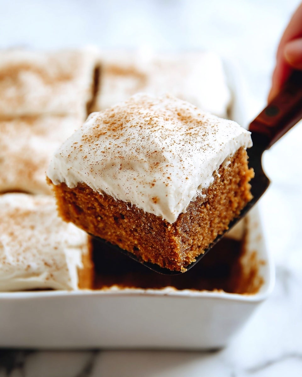 A close-up of a square piece of cake being lifted by a woman's hand holding a spatula. The cake has two layers: a thick, dark brown bottom layer with a soft, moist texture, and a thick top layer of creamy, smooth white frosting sprinkled lightly with fine specks of brown spice. The cake piece is cut from a larger cake with similar square sections visible in a white baking dish below. The background is a white marbled texture. Photo taken with an iphone --ar 4:5 --v 7