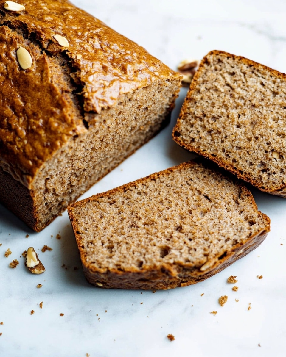 A loaf of bread with a golden brown crust is shown on a white marbled surface, with three slices cut from it and laid flat next to the loaf. The inside of the bread is light brown and speckled with small bits of walnuts or nuts. The crust has a shiny texture with a crack running along the top. There are some crumbs and small pieces scattered around the bread on the surface. photo taken with an iphone --ar 4:5 --v 6.1