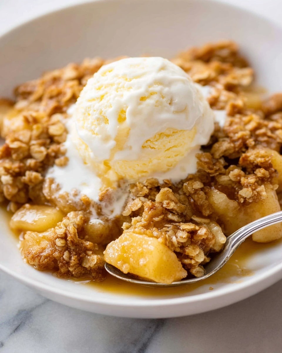 A close-up of a white bowl filled with warm apple crumble, showing a mix of golden brown oat topping with a crispy texture and soft, cooked apple pieces in a light caramel sauce beneath. On top, there is a single round scoop of creamy vanilla ice cream beginning to melt, creating white streaks that blend with the crumble below. A silver spoon rests in the bowl, partially visible in the background. The bowl sits on a white marbled surface. photo taken with an iphone --ar 4:5 --v 7
