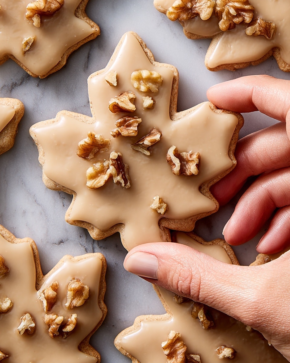 Several leaf-shaped cookies lay scattered on a white marbled surface. Each cookie has a smooth, light brown glaze covering the top, giving a shiny and even finish. Some cookies have small clusters of chopped nuts placed near the base or on one side, adding a rough texture contrast to the smooth glaze. The cookies have defined edges showing the leaf shape clearly, and the overall look is neat and inviting. Photo taken with an iphone --ar 4:5 --v 7