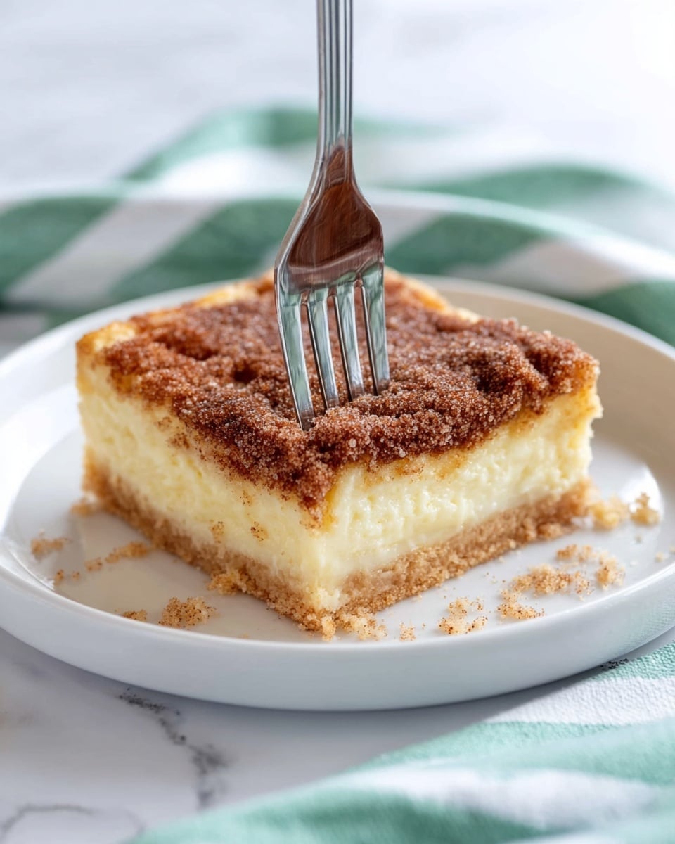 Three square pieces of a layered dessert are stacked on top of each other on a white marbled surface. Each piece has three visible layers: a thin, light golden brown crust at the bottom, a thick creamy white middle layer, and a top layer covered with a coarse sprinkle of cinnamon and sugar, giving a textured, slightly rough brown appearance with glittering sugar crystals. The top piece shows a small bite taken out from its side, revealing the soft creamy inside. The lighting highlights the sugar crystals and the creamy texture inside, making the layers clear and inviting. Photo taken with an iphone --ar 4:5 --v 7