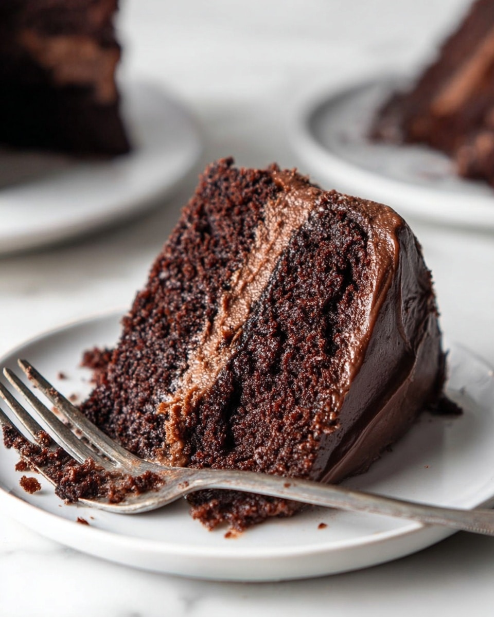 A slice of three-layer chocolate cake sits on a white plate with a silver fork beside it. The cake layers are dark brown and moist with a slightly crumbly texture. Between the layers, there is a smooth, lighter brown chocolate filling. The cake is covered in a dark chocolate frosting that is thick and creamy, wrapping the sides and top. The background shows a white marbled texture and blurred parts of other white plates with similar cake slices. Photo taken with an iphone --ar 4:5 --v 7
