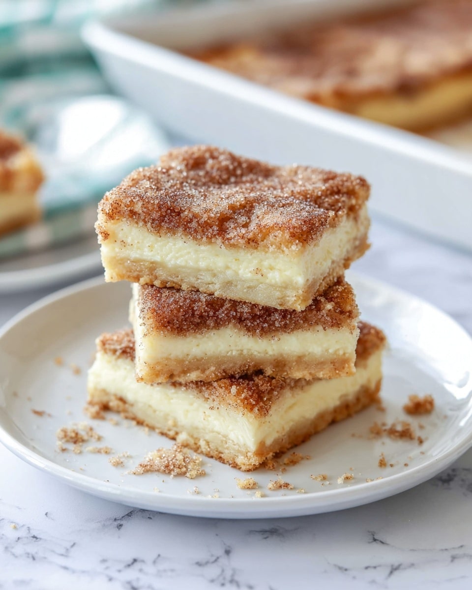There is a stack of three square pieces of a dessert on a white plate. Each piece has three layers: a light golden brown crust at the bottom, a thick creamy light yellow middle filling, and a top layer covered with a brown sugary cinnamon coating that looks slightly crunchy. The edges look soft but firm, and a few crumbs are scattered around the plate. The background has a white marbled texture, and a white dish can be seen blurred in the back, with a green and white striped cloth near the plate. The photo taken with an iphone --ar 4:5 --v 7