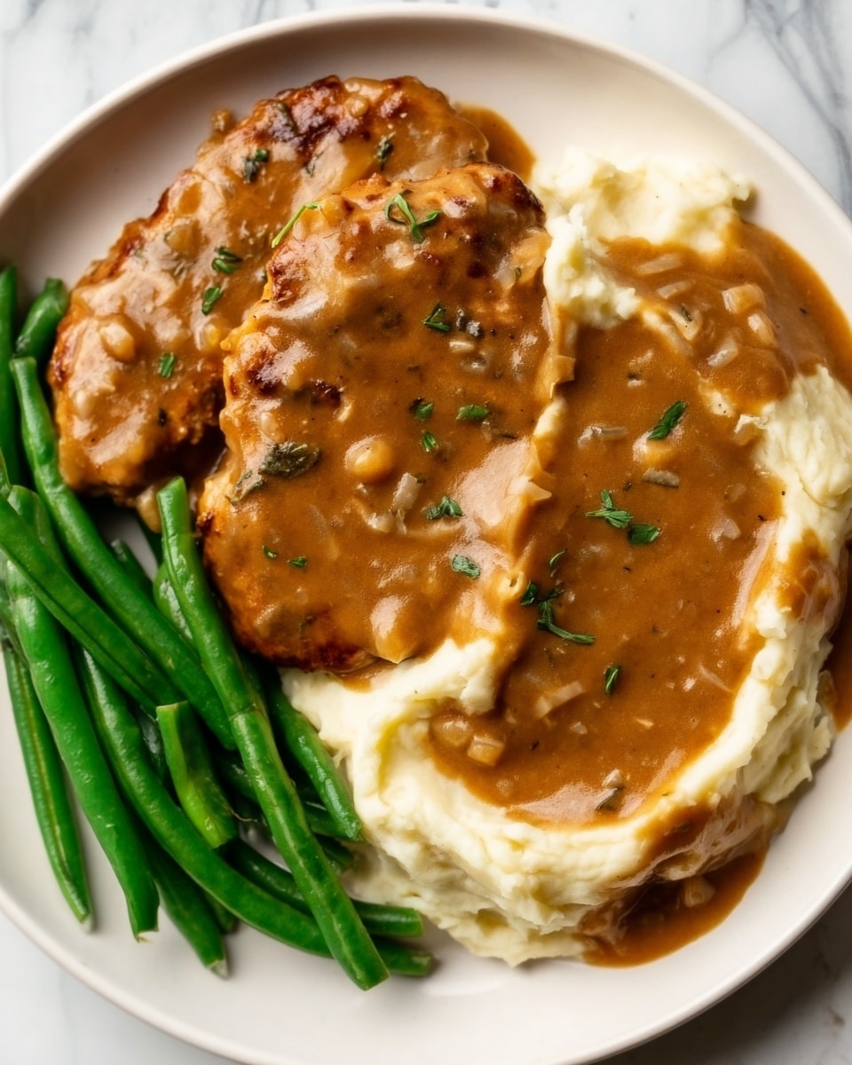 The dish shows two pieces of golden brown cooked chicken covered with thick brown gravy on the right side of a white plate; next to the chicken, there is a bed of creamy white mashed potatoes also topped with brown gravy with some visible bits of herbs on top; on the left side of the plate, there is a small pile of bright green cooked green beans arranged neatly; the plate is placed on a white marbled surface. photo taken with an iphone --ar 4:5 --v 7