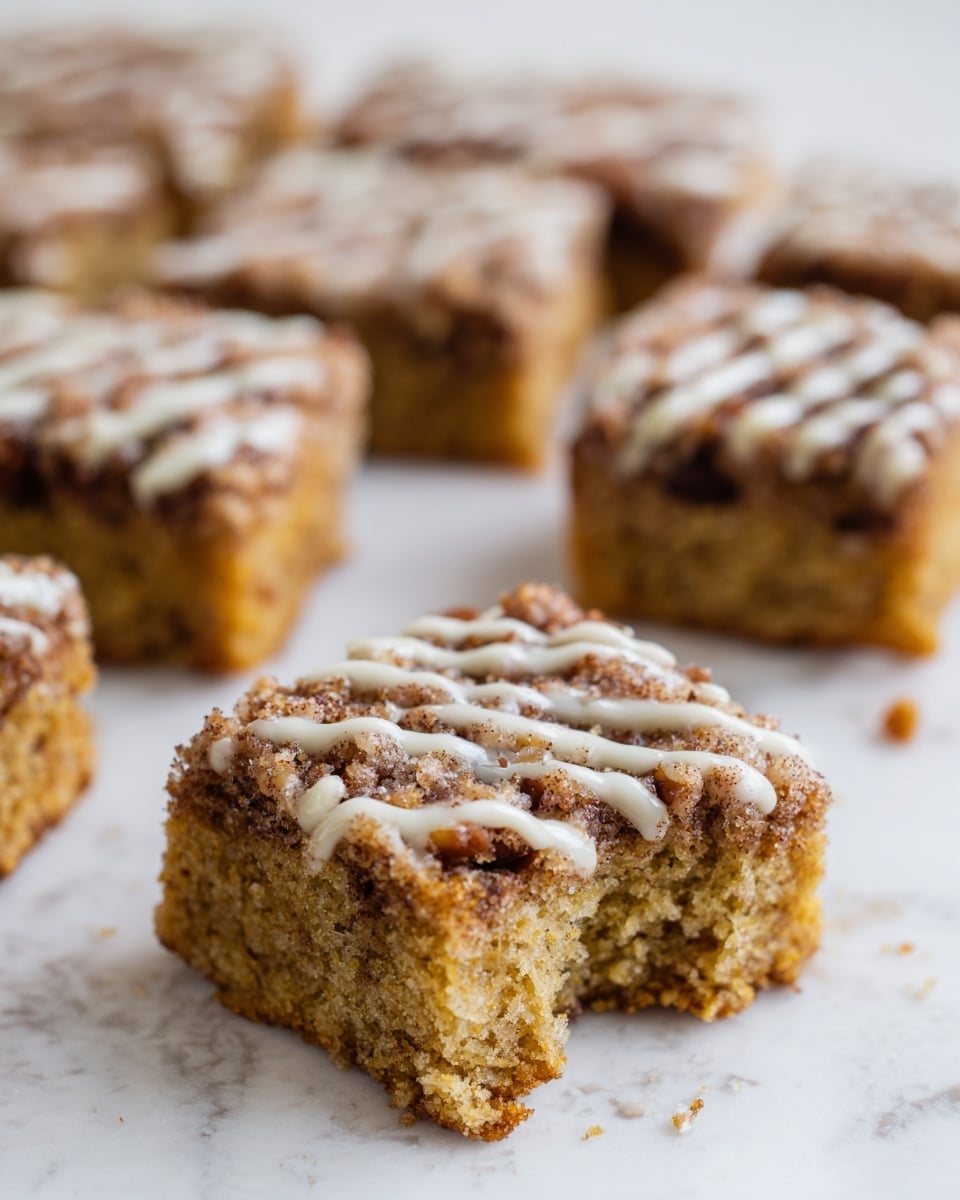 The image shows several square pieces of a brown cake with a crumbly, light texture. Each piece has a visible layer of chopped nuts and a drizzle of white icing on top. The cake squares are placed on a surface with white marbled texture. One piece in the front has a bite taken out, showing the soft inside and some nuts inside the cake as well. The other squares are whole and arranged closely behind the bitten piece. Photo taken with an iphone --ar 4:5 --v 7