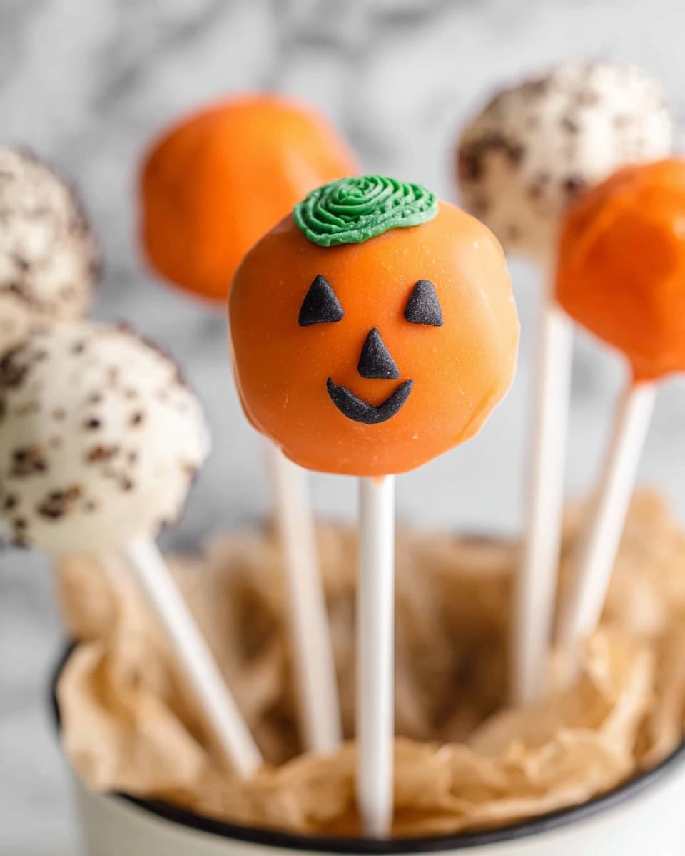 The image shows a group of Halloween-themed cake pops arranged in a clear glass bowl filled with light brown shredded paper. The cake pops have three designs: white mummy with white icing wrapped unevenly and two small round eyes on the front; orange pumpkin with a smooth orange coating, a small green stem on top, and a simple black smiling face; dark chocolate with a coating covered in small bright orange round sprinkles. The bowl is tied with a black ribbon with large white polka dots. The background is a soft white marbled texture, and the photo is taken with an iphone --ar 4:5 --v 7