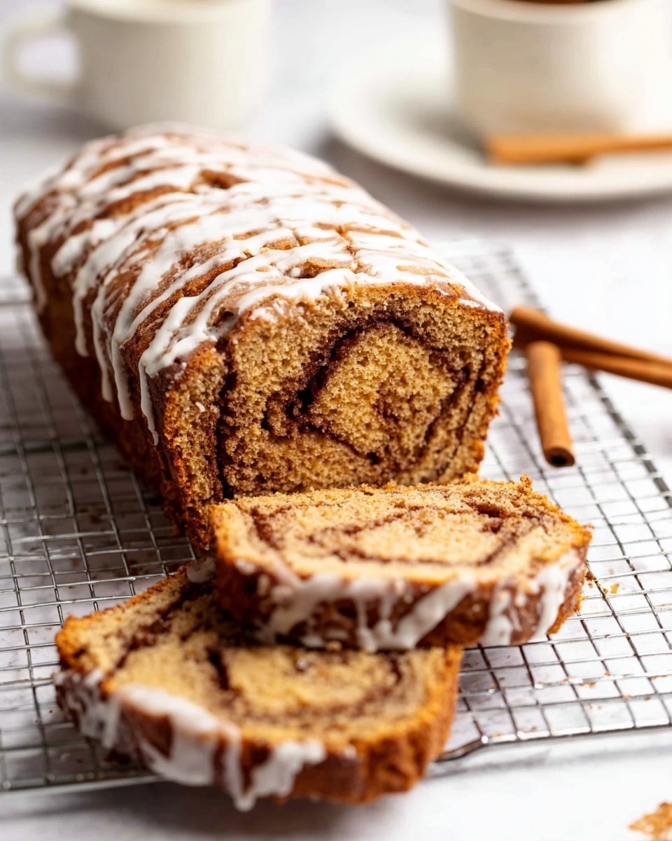 The image shows a loaf of cinnamon swirl bread with two slices cut and laid in front of it on a silver cooling rack. The bread has a golden-brown color with a darker brown cinnamon swirl pattern running through each slice, giving it a textured and soft appearance. A thin layer of white icing is drizzled over the top and sides of the bread and slices, adding a glossy contrast to the warm tones. The background features a white marbled surface, and a white plate with a cup and a cinnamon stick is blurred in the background. Photo taken with an iphone --ar 4:5 --v 7