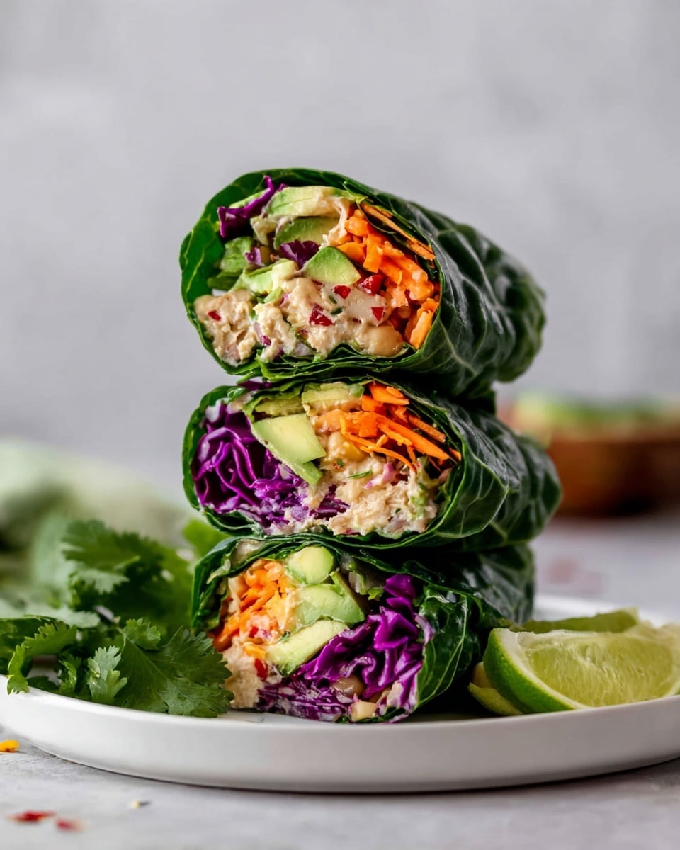 Three green leafy wraps are stacked on a white plate with lime wedges and fresh cilantro on the side, placed on a white marbled surface. Each wrap has a top layer of dark green leafy greens, under which there is a layer of thinly sliced bright purple cabbage and thin orange carrot sticks. Inside, there are chunks of light beige shredded filling mixed with small pieces of light green avocado. The textures of the filling are slightly crumbly and soft, contrasting with the crisp vegetables. photo taken with an iphone --ar 4:5 --v 7