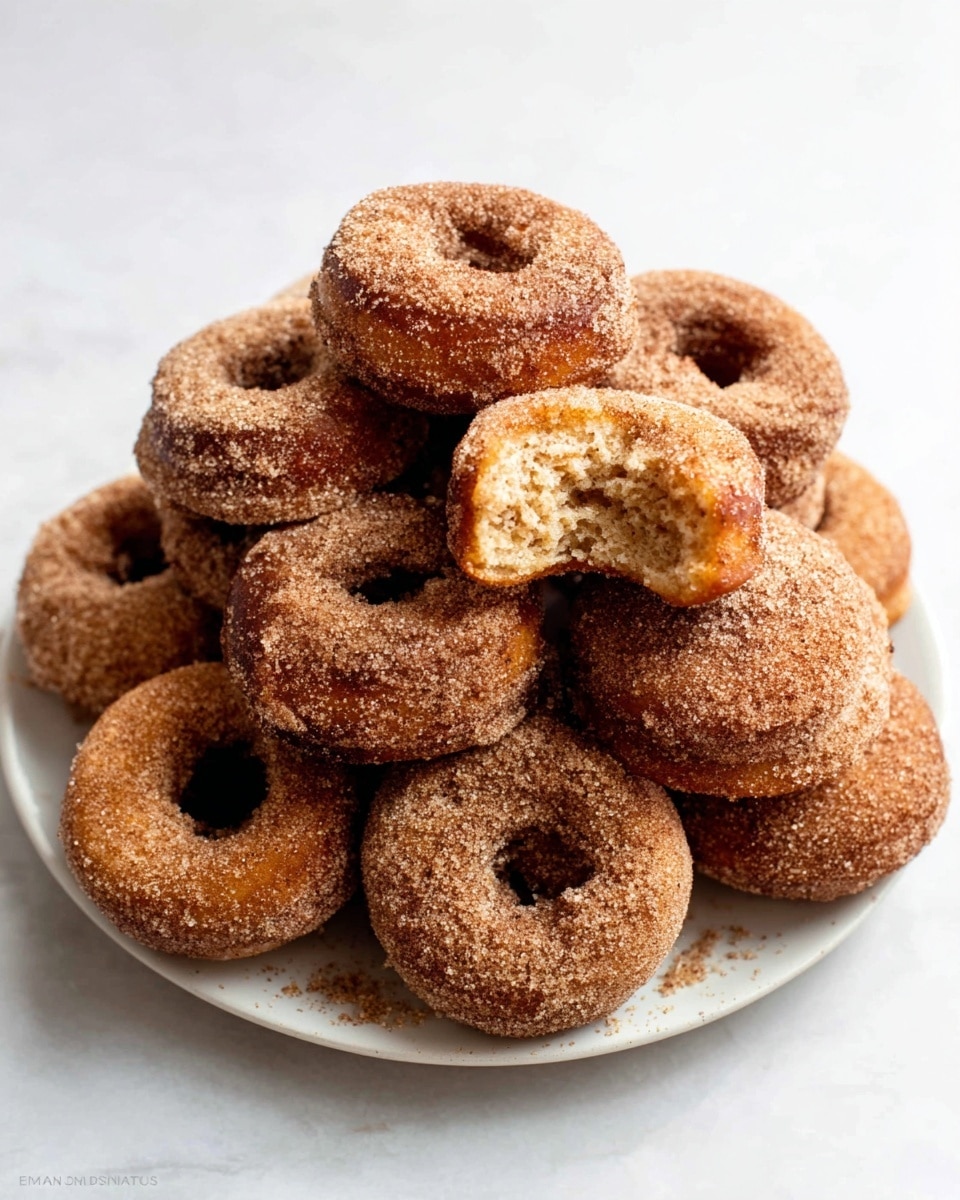 The image shows four brown sugar-coated donut holes stacked in a small pile on a white marbled surface. Three donut holes form a base with one balanced on top, and a single whole donut hole leans against the stack on the right side. To the left, two donut holes are broken open, revealing a soft, light brown inside texture. The sugar coating on each donut hole glistens slightly, highlighting their rough, grainy texture. The background is plain white. Photo taken with an iphone --ar 4:5 --v 7