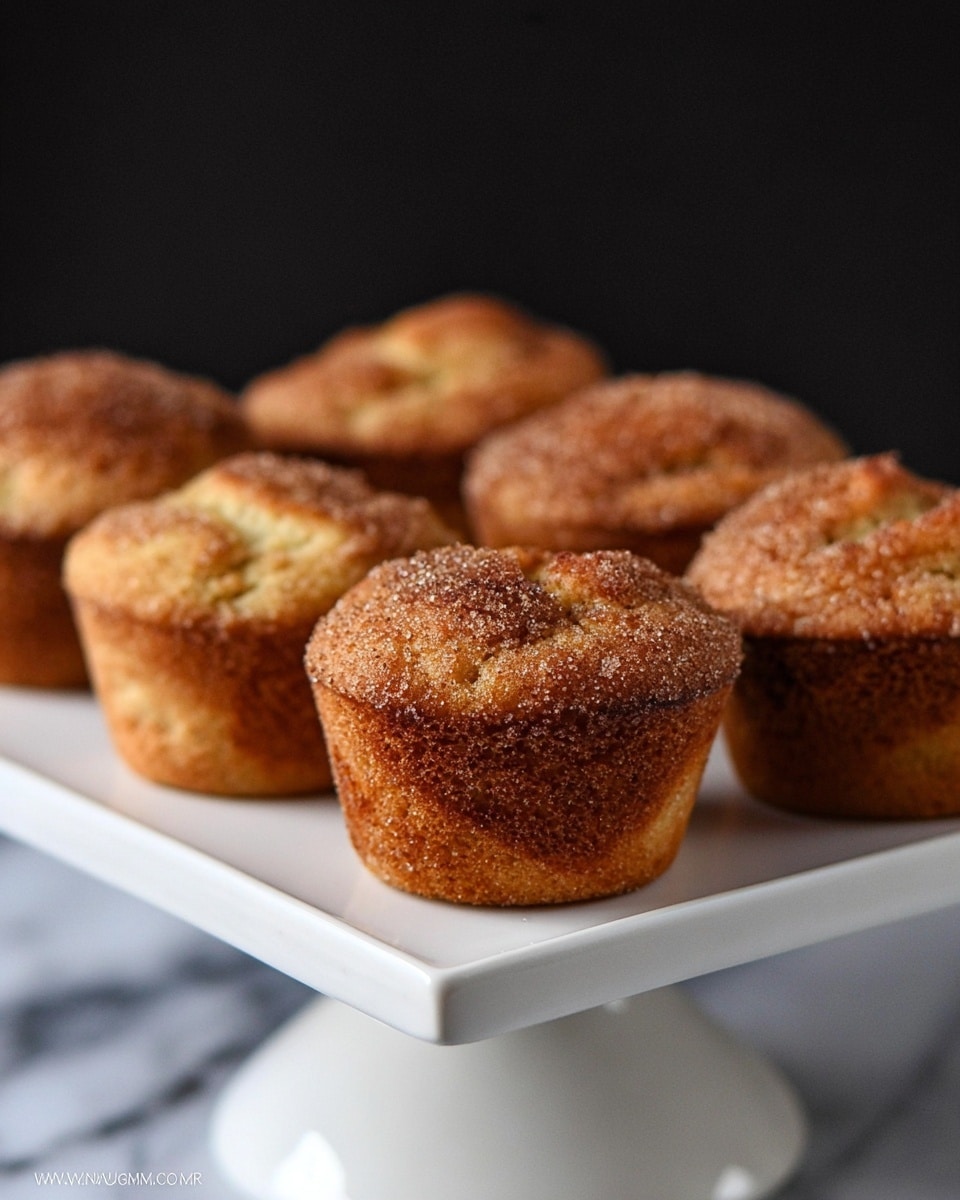 A close-up view of a single muffin with a golden-brown top dusted evenly with coarse cinnamon sugar, showing a slightly cracked surface that reveals its soft, light-yellow inside. The muffin appears fluffy with a rough texture and small visible crumb details on the side. It is placed on a white marbled surface, with no other objects in sight. The image focuses tightly on the muffin's top and upper side, highlighting the sugary topping and warm baked color photo taken with an iphone --ar 4:5 --v 7