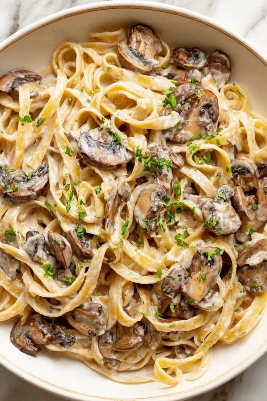 A close-up view of creamy mushroom pasta served in a white bowl. There are two main layers: soft fettuccine noodles coated in a light cream sauce forming the base layer, and tender mushroom slices mixed throughout on top. The mushrooms have a slightly darker brown color and a smooth, cooked texture. Small bits of green herbs are sprinkled over the pasta, adding a fresh touch. The bowl is placed on a white marbled surface. photo taken with an iphone --ar 2:3 --v 7 - Creamy Mushroom Pasta, Creamy Mushroom Pasta Recipe, Easy Mushroom Pasta, Garlic Mushroom Pasta, Vegetarian Mushroom Pasta