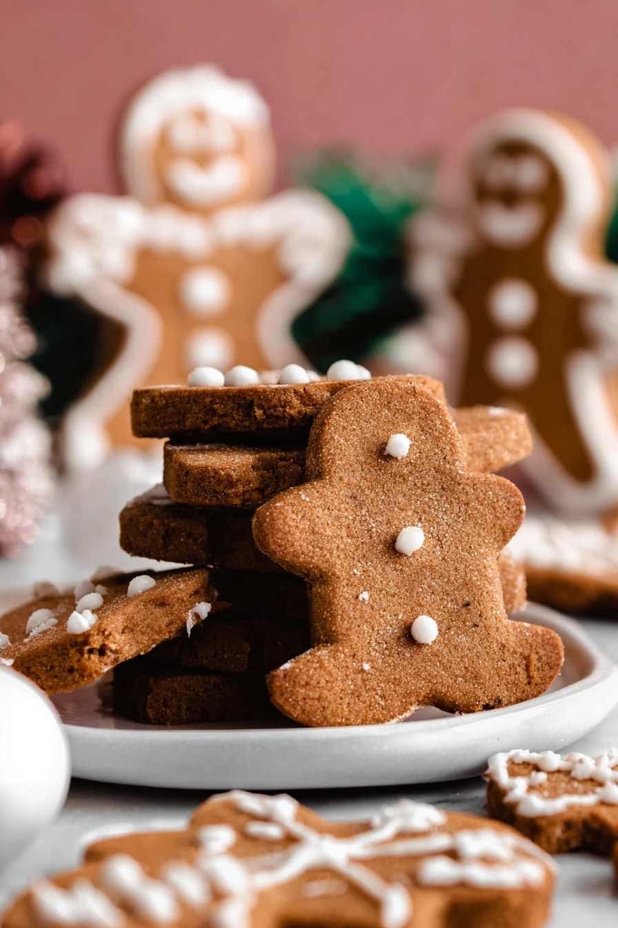 A close-up image of a stack of three uneven gingerbread cookies with a rough brown texture and white icing dots on top, placed on a white plate. Around the stack are more gingerbread cookies lying flat, decorated with white icing in simple patterns. In the background, there are two blurred gingerbread people standing upright with white icing details on a white marbled surface. A white Christmas ornament ball is visible near the plate's edge. The colors are warm, with brown tones from the cookies and subtle pink and green blurred backgrounds. Photo taken with an iphone --ar 2:3 --v 7 - Soft Gingerbread Cookies, gingerbread cookies, soft cookie recipes, holiday cookies, spiced cookie recipe