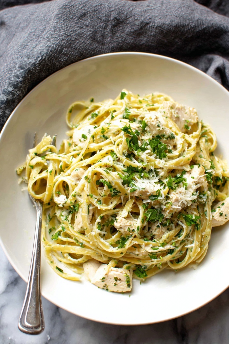 A white deep plate holds a serving of pasta with creamy sauce. The pasta is light yellow and twisted around itself in two layers, mixed with white pieces of chicken and sprinkled with bright green chopped herbs and grated cheese. A silver fork is placed partly in the pasta, resting in the bowl. The plate is set on a white marbled surface with a grey cloth nearby. Photo taken with an iphone --ar 2:3 --v 7 - Creamy Chicken Broccoli Alfredo, easy chicken and broccoli pasta, quick weeknight dinner, homemade Alfredo sauce, healthy creamy pasta
