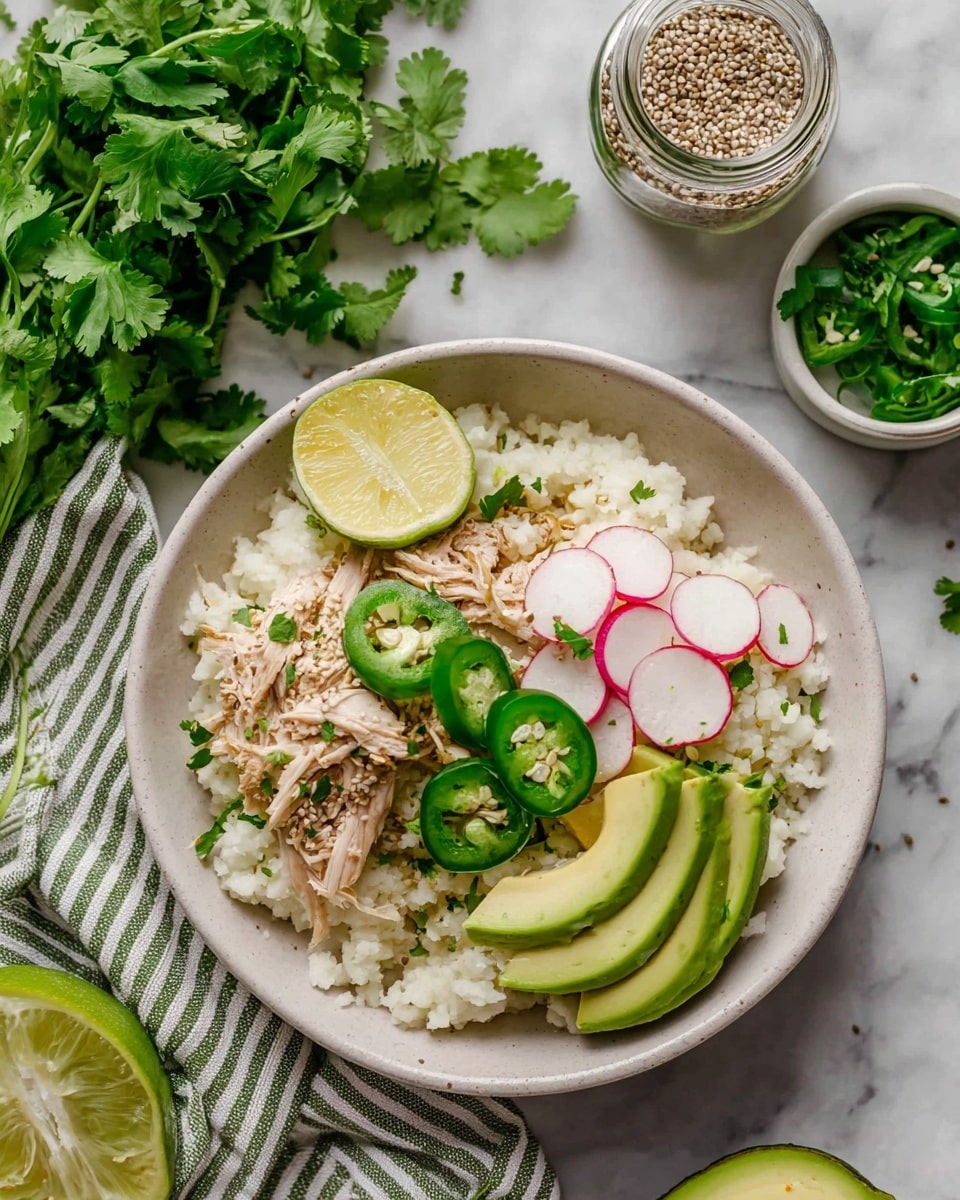 A white bowl contains a layered dish starting with a base of white rice shaped in a mound. On top, there is shredded light brown meat arranged loosely in the middle. On one side, bright green slices of avocado overlap each other neatly, while on the other side, thin round slices of pink-edged radish are placed. Several round slices of green jalapeño are scattered on top of the meat and avocado. A small wedge of pale yellow lemon rests at the top edge of the bowl. The dish is sprinkled with chopped green herbs and cracked black pepper. The bowl is set on a white marbled surface with fresh green cilantro, a jar of spices, and a lime partially visible nearby, with a black-and-white striped cloth under the bowl. Photo taken with an iphone --ar 4:5 --v 7