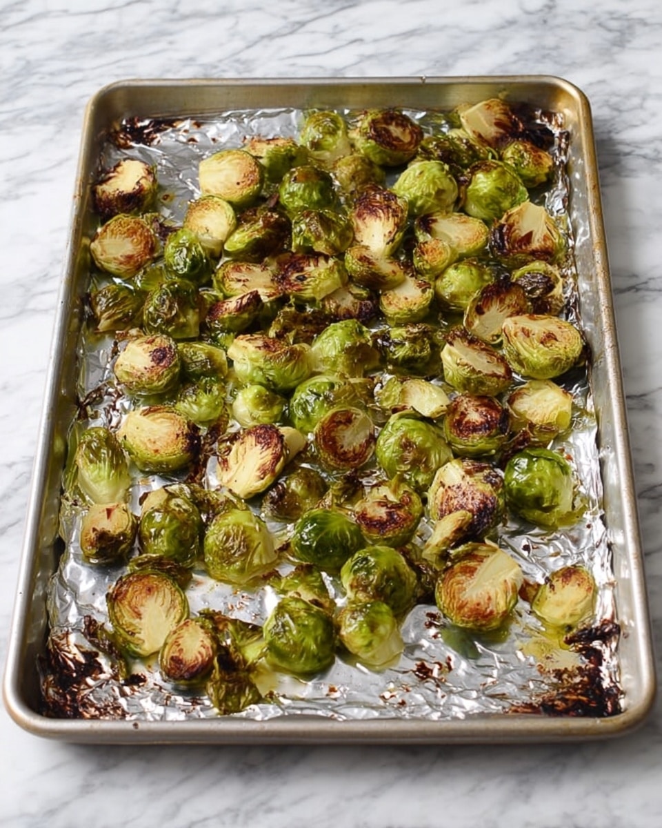 A metal baking sheet lined with shiny silver foil holds a single layer of roasted Brussels sprouts, some halved and some whole, spread across the tray. The Brussels sprouts have a mix of bright green and golden brown colors with crispy, slightly charred edges, showing a cooked texture that is both soft and crunchy. The baking sheet sits on a white marbled surface. Photo taken with an iphone --ar 4:5 --v 7