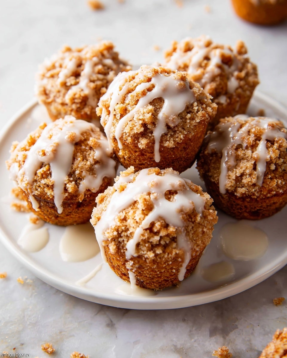 A close-up of five crumb muffins on a white marbled surface, each with a golden brown base wrapped in a beige paper liner; the muffins have a thick crumbly topping with light golden chunks, and a glossy white glaze drizzled unevenly over the top of the crumb layer, some crumbs scattered around the muffins. photo taken with an iphone --ar 4:5 --v 7