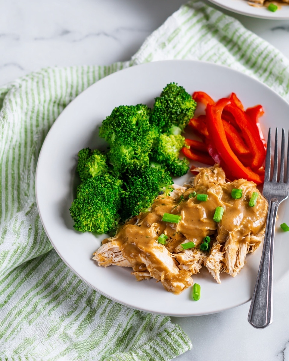 A white plate with three main parts: on the left, bright green broccoli pieces mixed with sliced green onions; below the broccoli, several slices of shiny red bell pepper; on the right, shredded light brown chicken topped with smooth brown sauce and small chopped green onions. A silver fork rests on the right edge of the plate. The plate sits on a white marbled surface with a green and white striped cloth beneath it. In the top right corner, part of another white plate with broccoli is visible. Photo taken with an iphone --ar 4:5 --v 7