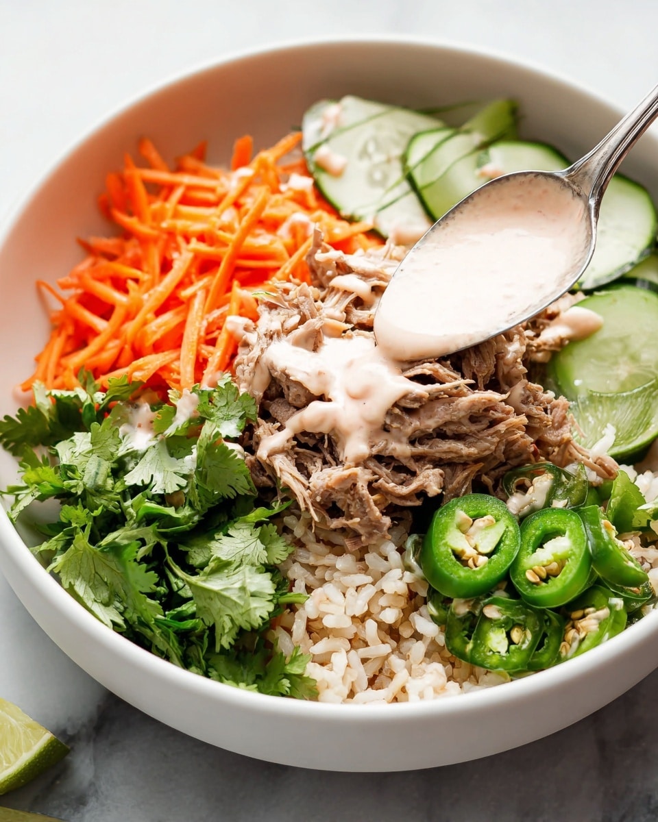 The dish is served in a white bowl on a white marbled surface, with a layer of brown rice at the bottom. On top, there is a pile of shredded cooked chicken in the center, drizzled with white sauce. On the left side, there are thin orange carrot strips mixed with some red pieces, with fresh green cilantro leaves above them. To the right, slices of green cucumber are arranged neatly in a fan shape. A few slices of green chili pepper are placed on top of the chicken, and two lime wedges rest on the right edge of the bowl. The overall look is fresh and colorful, with a soft focus background showing more bowls and sauce in small white containers. Photo taken with an iphone --ar 4:5 --v 7