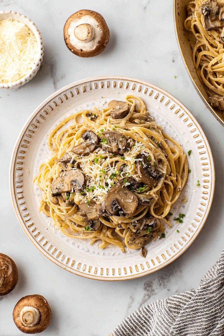 A round white plate with a raised dotted edge holds a serving of pasta with mushrooms. The pasta is light brown and tangled in the center of the plate. Several brown mushroom slices are mixed evenly with the pasta. The dish is topped with small green herb pieces and sprinkled with thin white cheese flakes. Around the plate, the surface is a white marbled texture with some whole mushrooms nearby and a small white bowl with white cheese flakes on the left. A striped cloth partially visible on the right side holds a white pan with more of the same mushroom pasta dish inside. photo taken with an iphone --ar 2:3 --v 7 - Creamy Mushroom Pasta, Creamy Mushroom Pasta Recipe, Easy Mushroom Pasta, Garlic Mushroom Pasta, Vegetarian Mushroom Pasta