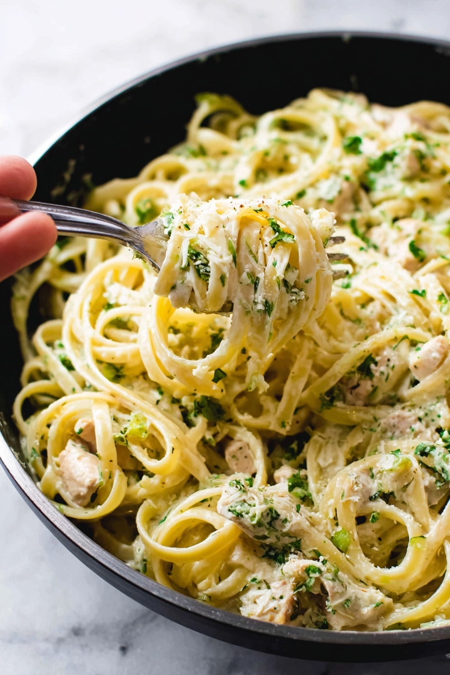 The image shows a white bowl filled with a pasta dish placed on a gray cloth over a white marbled surface. The pasta, likely fettuccine, is light yellow and mixed with small pieces of light-colored chicken. The dish is topped with finely chopped green herbs, which add a fresh touch. A metal fork is standing upright in the pasta, leaning on the edge of the bowl. The dish looks creamy with a slightly rough texture from the herbs, and the overall presentation is simple and appetizing. photo taken with an iphone --ar 2:3 --v 7 - Creamy Chicken Broccoli Alfredo, easy chicken and broccoli pasta, quick weeknight dinner, homemade Alfredo sauce, healthy creamy pasta