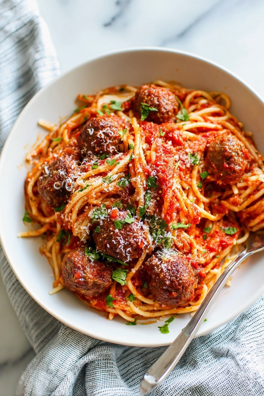 A white bowl filled with a serving of spaghetti noodles coated in red tomato sauce, topped with five browned meatballs evenly spaced on top. The spaghetti is mixed with green chopped herbs scattered across the dish, and a light sprinkle of grated white cheese adds texture on top of the meatballs and sauce. A silver fork rests inside the bowl on the left side, and the bowl sits on a white marbled surface with a soft blue and white striped cloth nearby. Photo taken with an iphone --ar 2:3 --v 7 - Easy Homemade Spaghetti and Meatballs, homemade spaghetti and meatballs recipe, best spaghetti and meatballs, quick pasta with meatballs, classic Italian spaghetti and meatballs