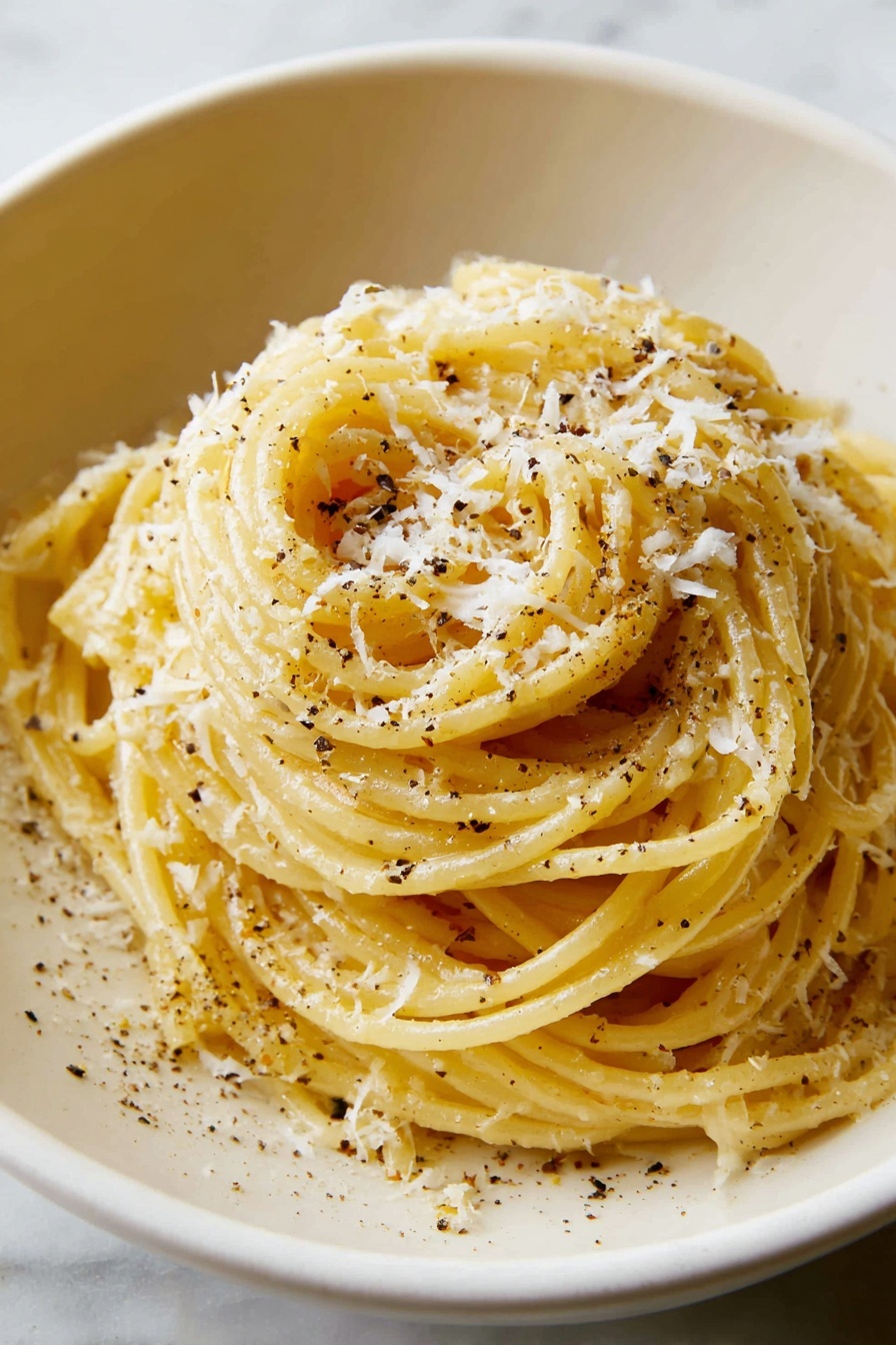 A white bowl filled with yellow spaghetti noodles tossed with specks of black pepper, topped with small white shavings of cheese. A fork held by a woman's hand lifts a portion of the spaghetti above the bowl, showing the smooth texture and slight shine of the noodles. Behind the bowl is a small white bowl containing grated cheese, set on a white marbled surface with a beige cloth partially visible on the left side. The background is soft and neutral, keeping the focus on the pasta dish. photo taken with an iphone --ar 2:3 --v 7 - Easy Cacio e Pepe Pasta, simple Cacio e Pepe recipe, quick pasta dinner, creamy cheese pasta, easy Italian pasta recipe