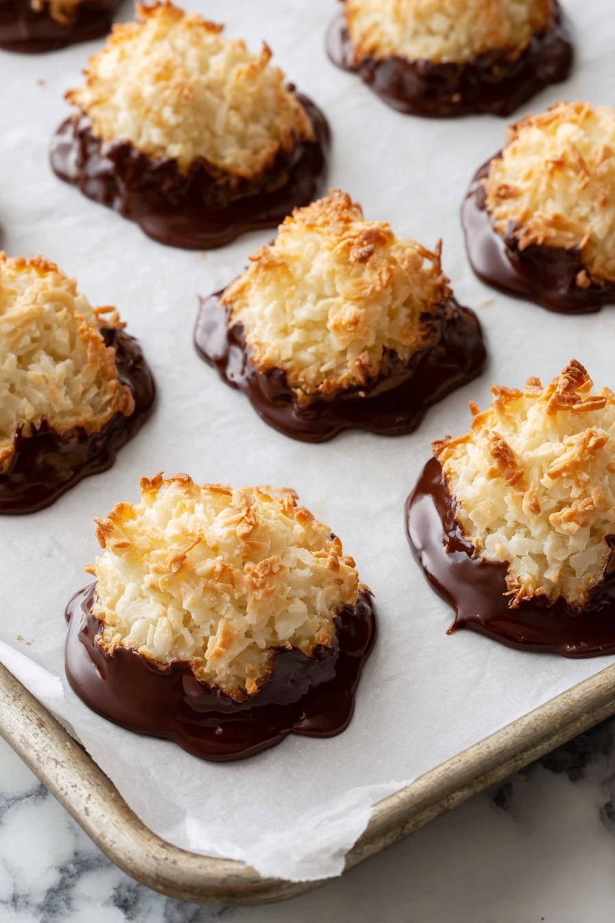 A white ceramic plate holds a pile of seven dome-shaped coconut macaroons. Each macaroon has two layers: the top layer is rough and light beige with toasted shredded coconut, and the bottom layer is covered in smooth, dark chocolate that looks glossy and slightly melted where it meets the coconut. The macaroons are stacked in a pyramid-like shape on the plate. The plate rests on a wooden table, with a colorful cloth with red, orange, blue, and green patterns blurred in the background. photo taken with an iphone --ar 2:3 --v 7 - Chocolate Dipped Coconut Macaroons, coconut macaroons with chocolate, easy coconut macaroon recipe, homemade coconut treats, chocolate-covered coconut cookies