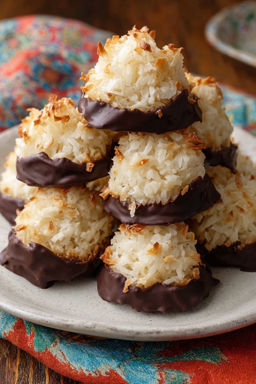 The image shows six round coconut cookies placed on white parchment paper on a metal tray with a white marbled texture surface underneath. Each cookie has two layers: the top is a rough-textured, golden-brown toasted coconut mound with a slightly uneven surface, and the bottom layer is a glossy, dark brown chocolate base that looks thick and melted, spreading slightly beyond the coconut layer's edges. The cookies are spaced out evenly, showing a contrast between the light coconut and dark chocolate. The photo taken with an iphone --ar 2:3 --v 7 - Chocolate Dipped Coconut Macaroons, coconut macaroons with chocolate, easy coconut macaroon recipe, homemade coconut treats, chocolate-covered coconut cookies