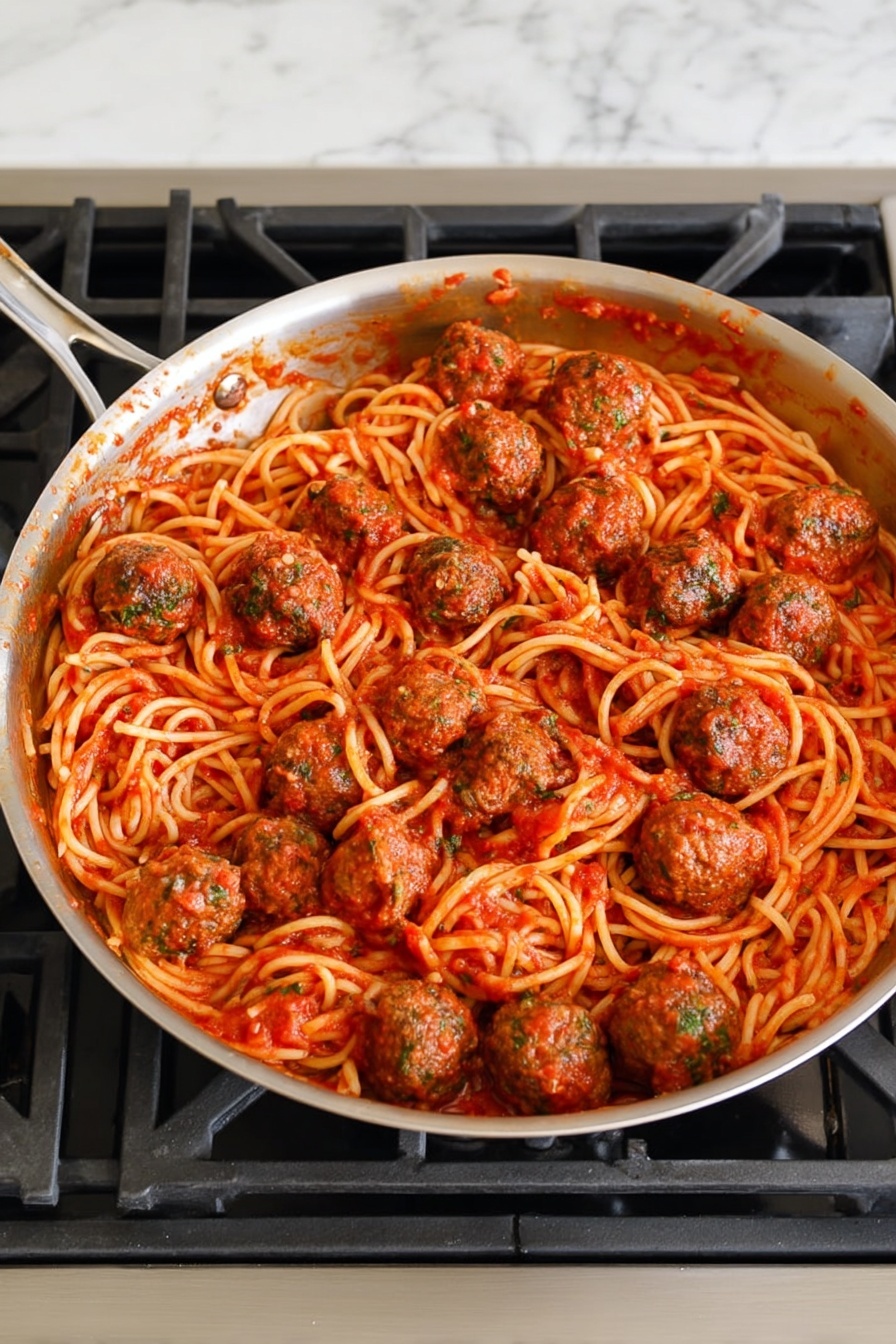 A shiny silver pan filled with a large amount of spaghetti pasta coated in bright red tomato sauce covers the bottom layer. On top of the spaghetti, there are many round, brown meatballs with bits of green herbs visible inside, spread evenly throughout the pan. The tomato sauce has a slightly chunky texture and lightly stains the sides of the pan. The pan rests on a black stove burner over a white marbled surface. photo taken with an iphone --ar 2:3 --v 7 - Easy Homemade Spaghetti and Meatballs, homemade spaghetti and meatballs recipe, best spaghetti and meatballs, quick pasta with meatballs, classic Italian spaghetti and meatballs
