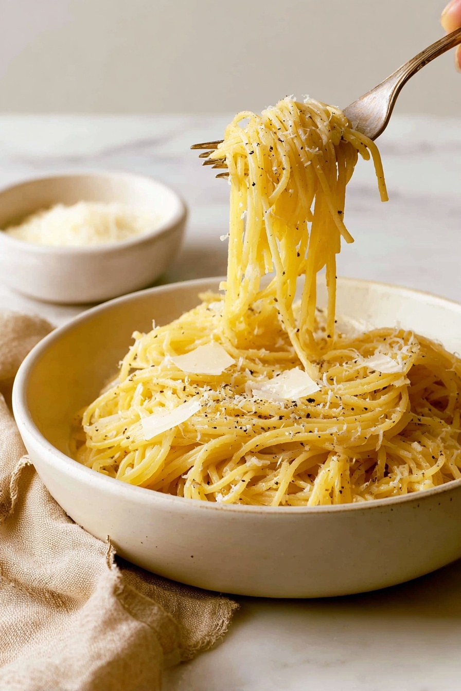 A white plate holds a single serving of spaghetti twirled into a loose mound in the center. The spaghetti is pale yellow with a slight shine from light oil or butter. On top, there is a light dusting of finely grated white cheese that contrasts with small black specks of ground pepper scattered evenly. A silver fork with a dark handle lies resting on the left side of the plate, partially under the spaghetti. The background and surface underneath have a white marbled texture. Photo taken with an iphone --ar 2:3 --v 7 - Easy Cacio e Pepe Pasta, simple Cacio e Pepe recipe, quick pasta dinner, creamy cheese pasta, easy Italian pasta recipe