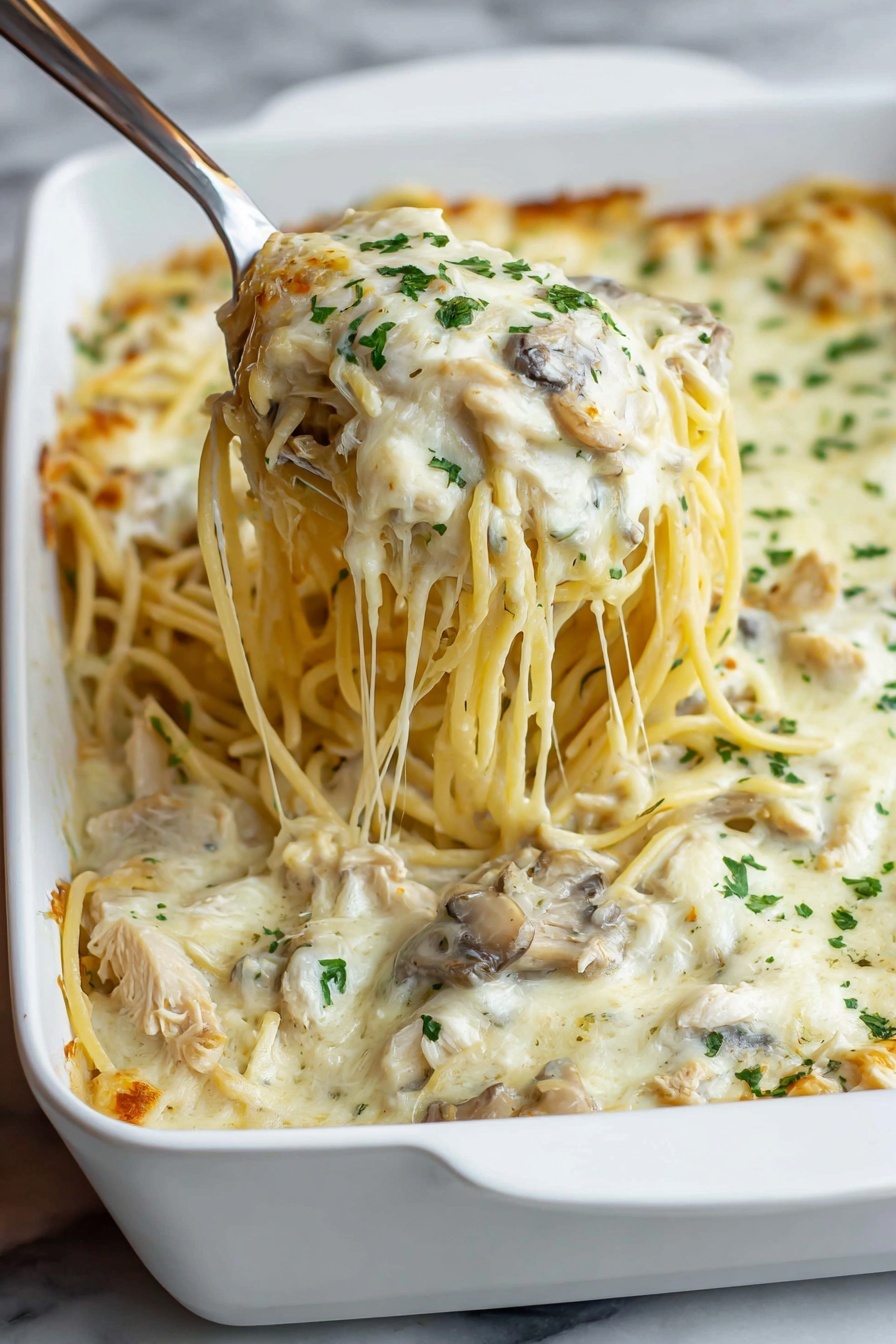 A white rectangular casserole dish filled with a layered baked pasta dish. The bottom layer consists of light yellow spaghetti noodles mixed with small pieces of brown mushrooms. The top layer is creamy white melted cheese, spread evenly with small browned spots and sprinkled with finely chopped green herbs. The edges of the noodles peek slightly through the cheese around the sides. The dish is placed on a wooden surface. photo taken with an iphone --ar 2:3 --v 7 - Creamy Chicken Tetrazzini Pasta Bake, easy chicken tetrazzini, cheesy pasta casserole, comforting chicken pasta, homemade tetrazzini recipe