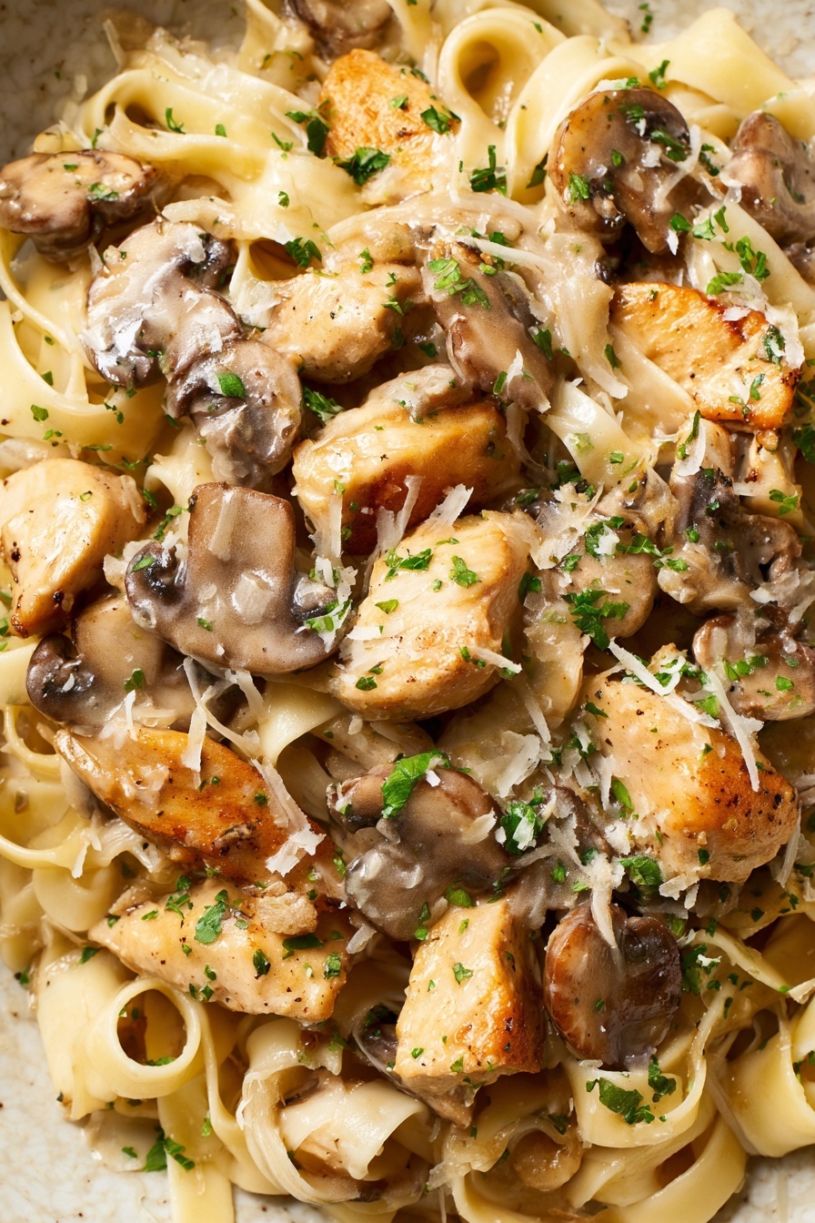 The image shows a close-up of a creamy pasta dish with three main layers: at the bottom are light beige, flat fettuccine noodles coiled and spread through the dish; on top of the pasta are golden-brown cooked chicken pieces that look tender and slightly crispy on the edges; mixed throughout and on top are slices of brown mushrooms with a soft texture. The dish is covered with a light creamy sauce that gives a slightly shiny look, sprinkled with small bits of green parsley and finely grated white cheese. The colors include light beige from the pasta and sauce, golden from the chicken, brown from the mushrooms, and bright green from the parsley, all on a white marbled textured surface. photo taken with an iphone --ar 2:3 --v 7 - Creamy Chicken Marsala Pasta, Chicken Marsala pasta recipe, easy Chicken Marsala pasta, quick creamy chicken pasta, gourmet chicken pasta dishes