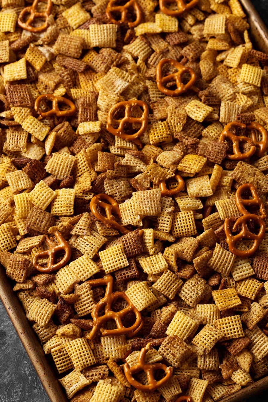 A large baking tray filled with a snack mix that has three main layers: light yellow square cereal pieces with a woven texture, small golden-brown pretzel shapes scattered across, and thin, rounded brown cracker pieces evenly mixed throughout. The snack mix layers blend together with a crunchy texture, sitting on a dark surface. The colors range from light yellow to brown and golden orange, creating a warm and inviting look. Photo taken with an iphone --ar 2:3 --v 7 - Homemade Chex Mix, Chex Mix recipe, savory snack ideas, homemade snack recipe, easy party snacks