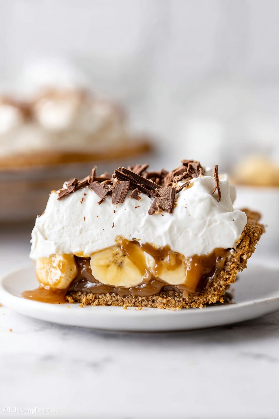 This image shows a close-up of a pie in a clear glass dish on a white marbled surface. The pie has four visible layers: a base layer of golden brown crumbly crust, a layer of light brown caramel filling, a thick layer of sliced pale yellow bananas, and a top layer of fluffy white whipped cream. The whipped cream is decorated with thin dark brown chocolate shavings scattered on top. Part of the pie is missing, revealing the inside layers clearly. The photo taken with an iphone --ar 2:3 --v 7 - Banoffee Pie with Dulce de Leche, best banana caramel pie, easy banoffee dessert, homemade dulce de leche pie, indulgent banana tart