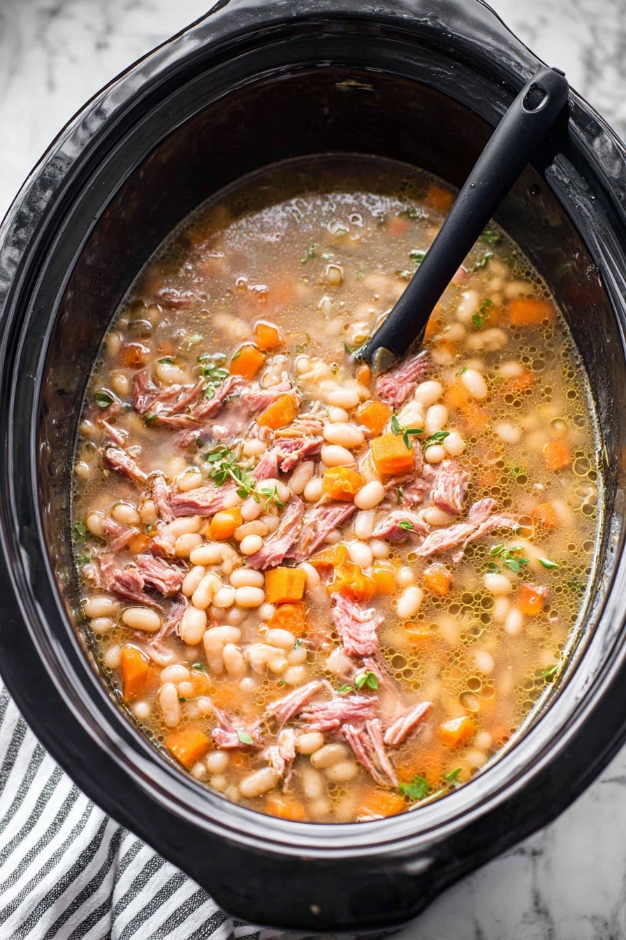 A large black slow cooker filled with a stew that has several layers and textures. The base layer shows a light brown broth with small bubbles of oil floating on top. Floating in the broth are many small, soft white beans, many small orange carrot cubes, and small bits of translucent onions. There are also shredded pieces of pinkish-brown cooked meat spread evenly throughout. Small green herbs are scattered on top, adding a fresh touch. A black spoon is partially submerged on the left side, resting inside the slow cooker. The slow cooker sits on a white marbled surface with a striped cloth partially visible below. Photo taken with an iphone --ar 2:3 --v 7 - Hearty Ham and Bean Soup, hearty ham and bean soup, smoky ham bean soup, comforting bean and ham stew, easy ham and bean dish