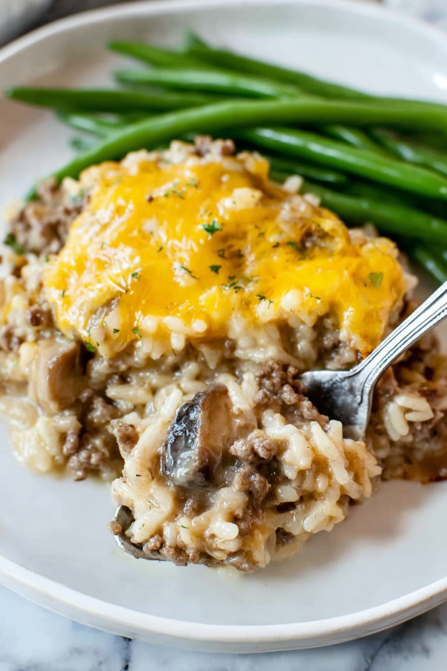 The dish shows two main layers on a white plate with green beans at the back. The bottom layer is a mix of cooked rice, ground meat, and slices of mushrooms, all combined in a creamy sauce with a light brown color and soft texture. The top layer is a covering of melted yellow cheese, unevenly spread, adding a slightly shiny and smooth look. The green beans are long and firm, bright green, placed behind the main dish. A silver fork is lifting a spoonful from the bottom layer, showing the mix of rice, meat, and mushrooms clearly. The plate is set on a white marbled surface photo taken with an iphone --ar 2:3 --v 7 - Cheesy Ground Beef and Rice Casserole, easy ground beef casserole, cheesy dinner recipe, quick one-pot casseroles, comforting beef and rice dish